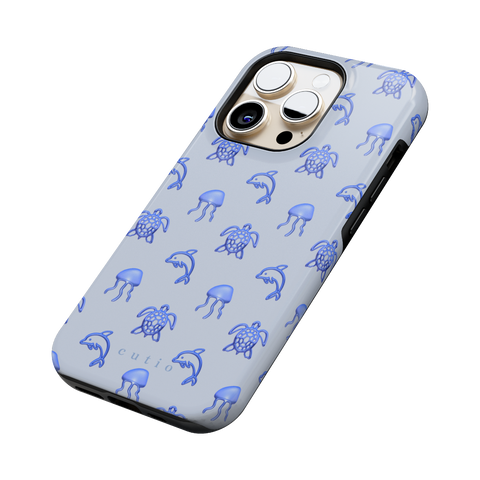 Blue Drift tough phone case featuring glossy blue turtles, dolphins, and jellyfish floating on a cool pale blue background, side view on iPhone